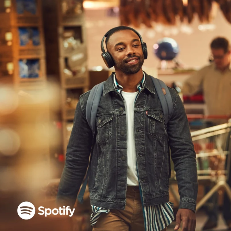 Man smiling while walking and listening to music with Spotify logo visible on his headphones