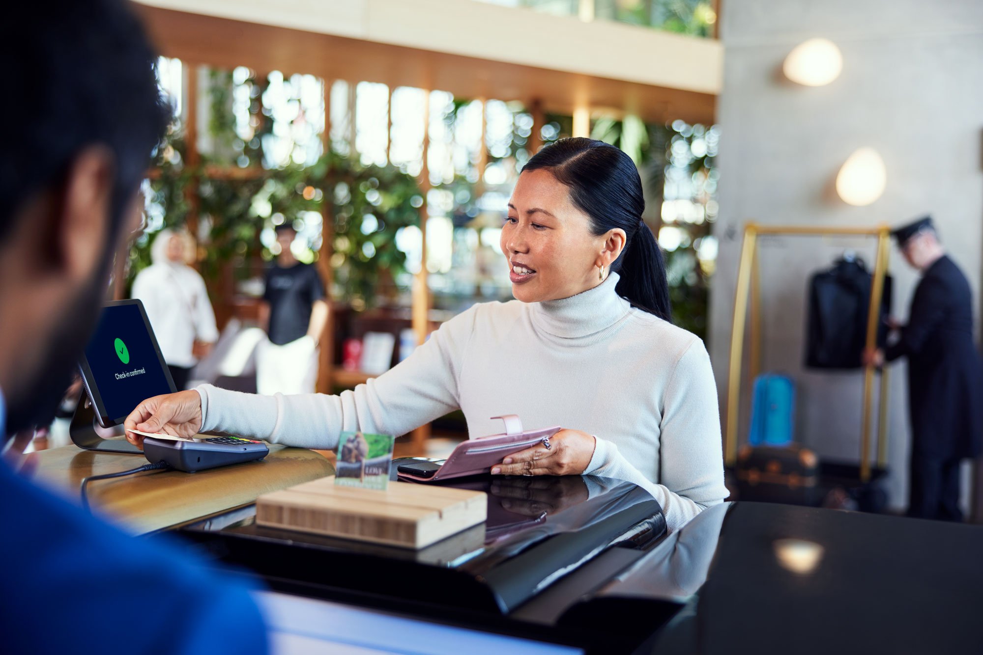 Una mujer en el mostrador de recepción de un hotel pagando su estancia tocando una tarjeta en el terminal de Adyen.
