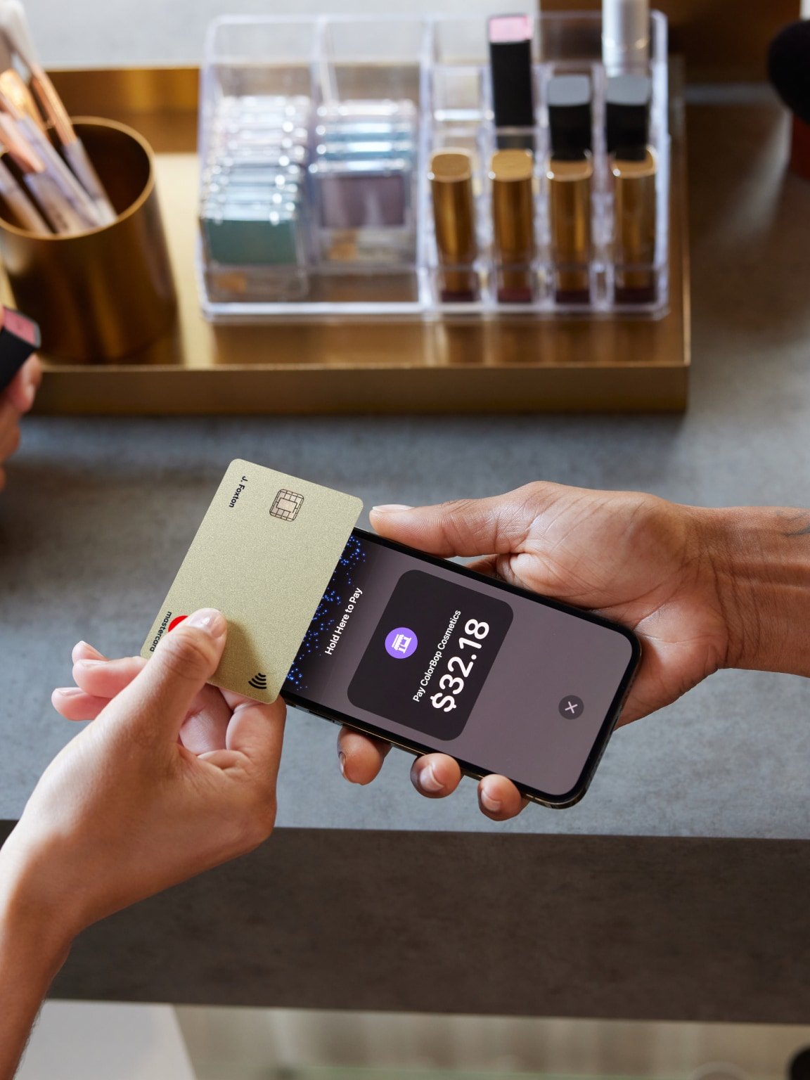 Close-up of a contactless payment being made using a gold card and a smartphone displaying the transaction amount.