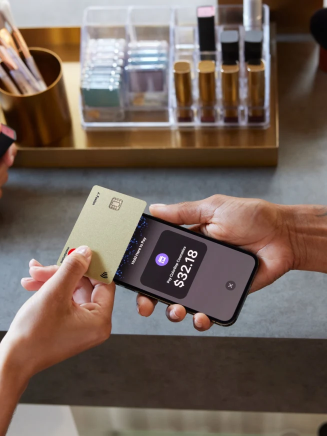 Close-up of a contactless payment being made using a gold card and a smartphone displaying the transaction amount.