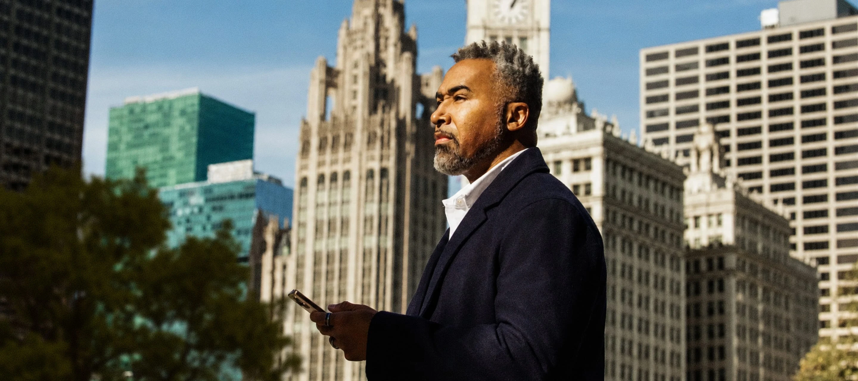 Businessman using a smartphone outdoors with city skyscrapers in the background.