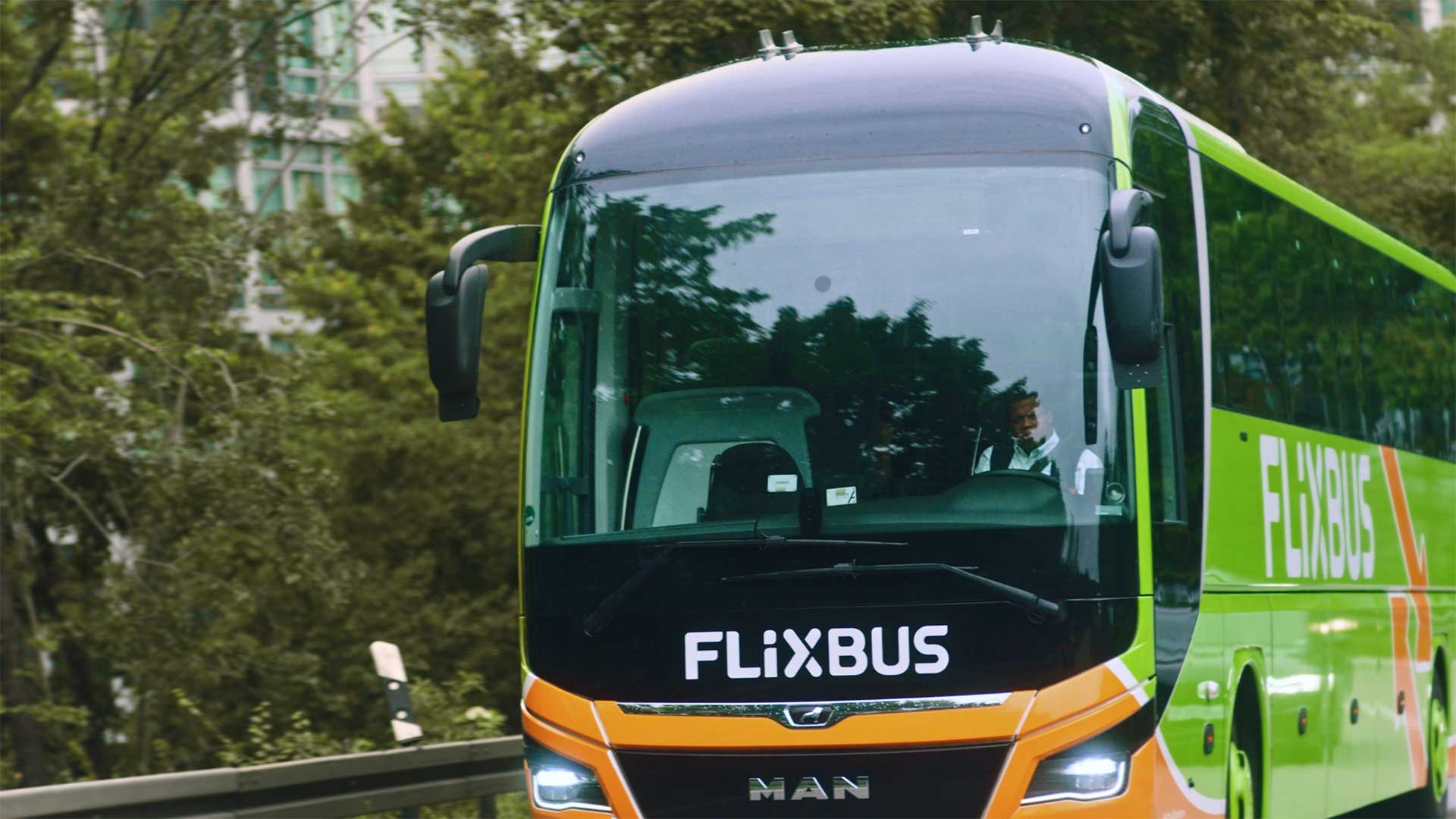 Grønt og orange Flixbus køretøj med en synlig chauffør gennem forruden.