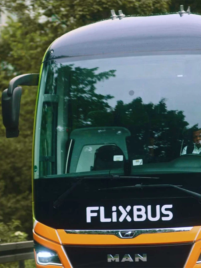 Grønt og orange Flixbus køretøj med en synlig chauffør gennem forruden.