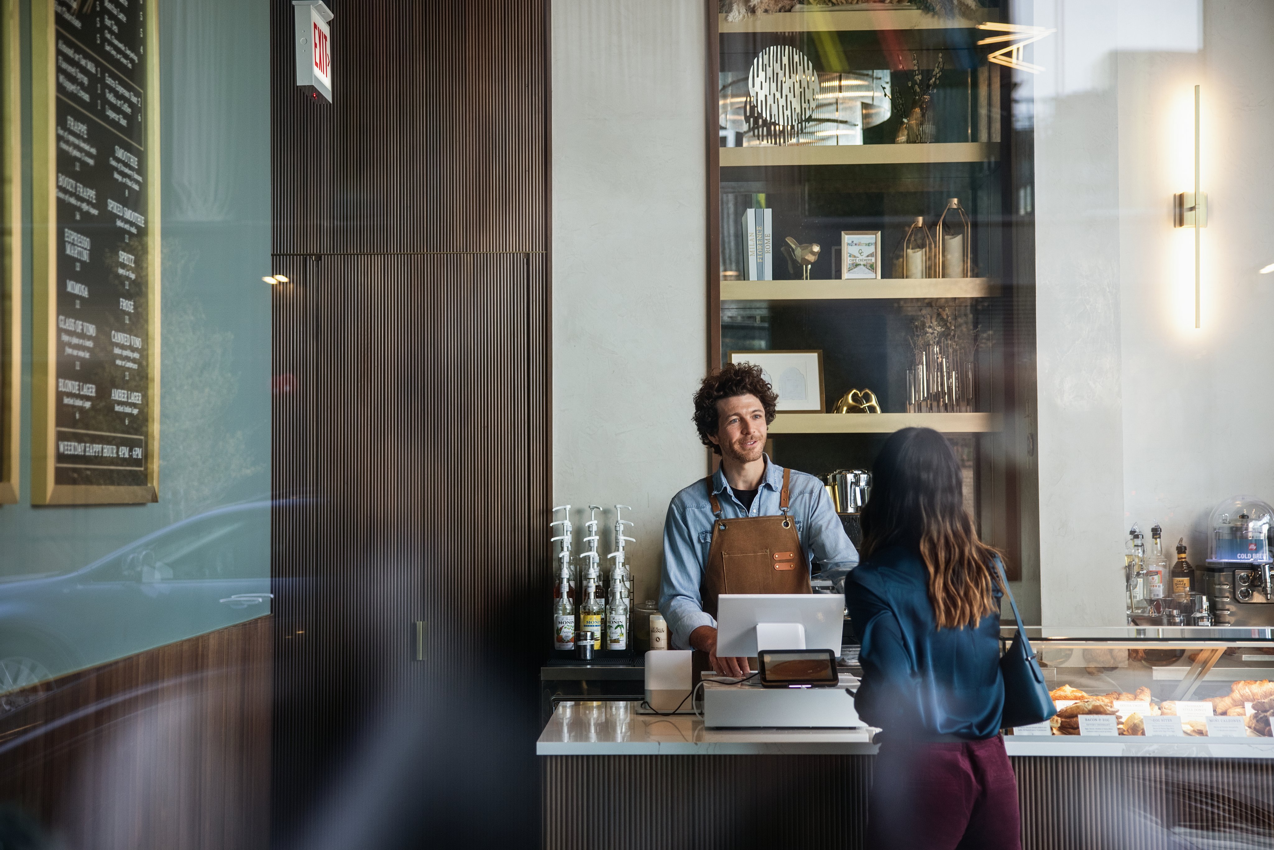 Adyen team members assist a customer at the counter in a modern cafe setting
