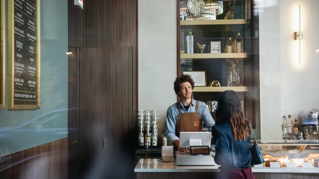 Adyen team members assist a customer at the counter in a modern cafe setting