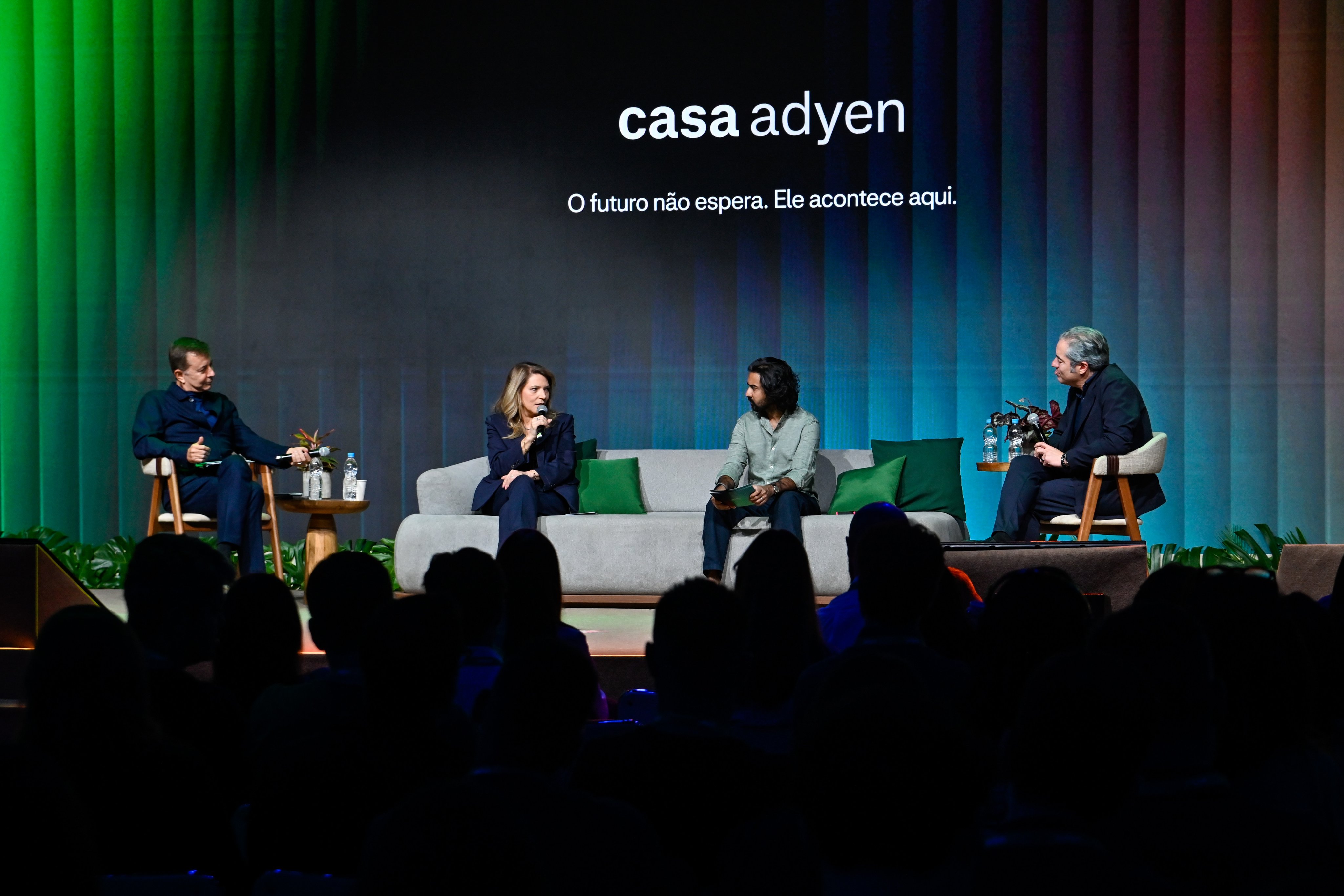 Membros da equipe Adyen conversam durante painel com apresentação ao fundo, demonstrando colaboração empresarial.