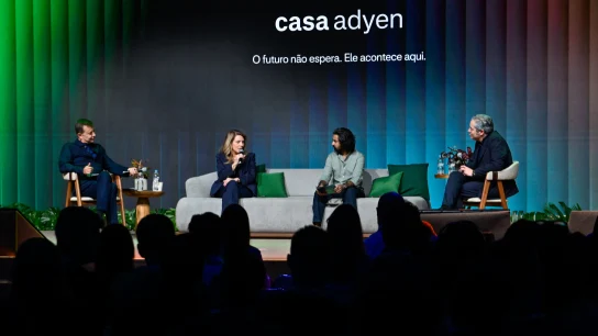 Membros da equipe Adyen conversam durante painel com apresentação ao fundo, demonstrando colaboração empresarial.