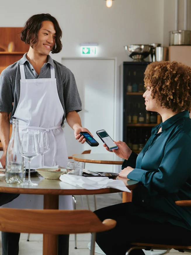 Una coppia in un ristorante paga il cibo toccando uno smartphone sul terminale AMS1 di Adyen