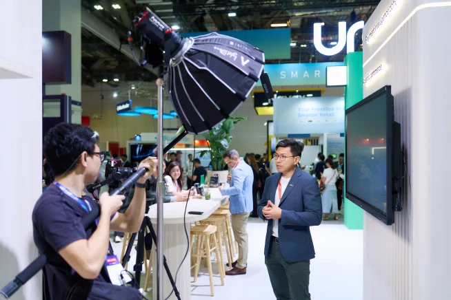Adyen team member filming a presentation at a trade show booth with an Adyen payment terminal.
