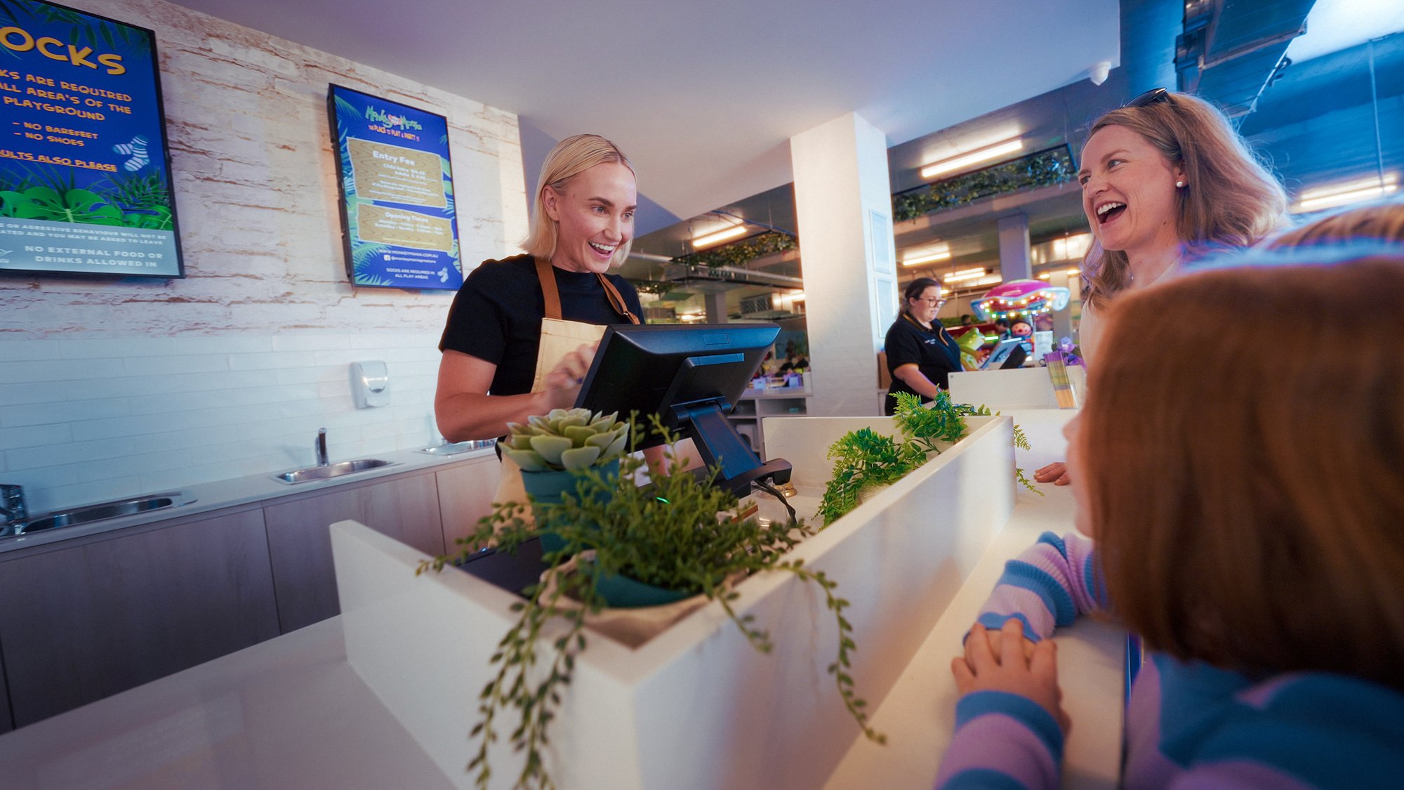 A customer and child at a checkout counter with an Adyen payment terminal in a busy retail space