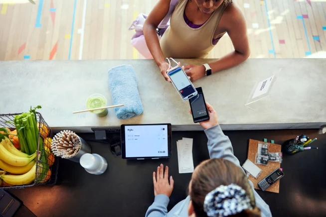 A woman at a gym paying by tapping her smartphone on Adyen's S1E terminal.