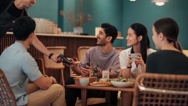 A man at a restaurant counter, paying for his order by tapping his phone on Adyen’s V400m terminal.