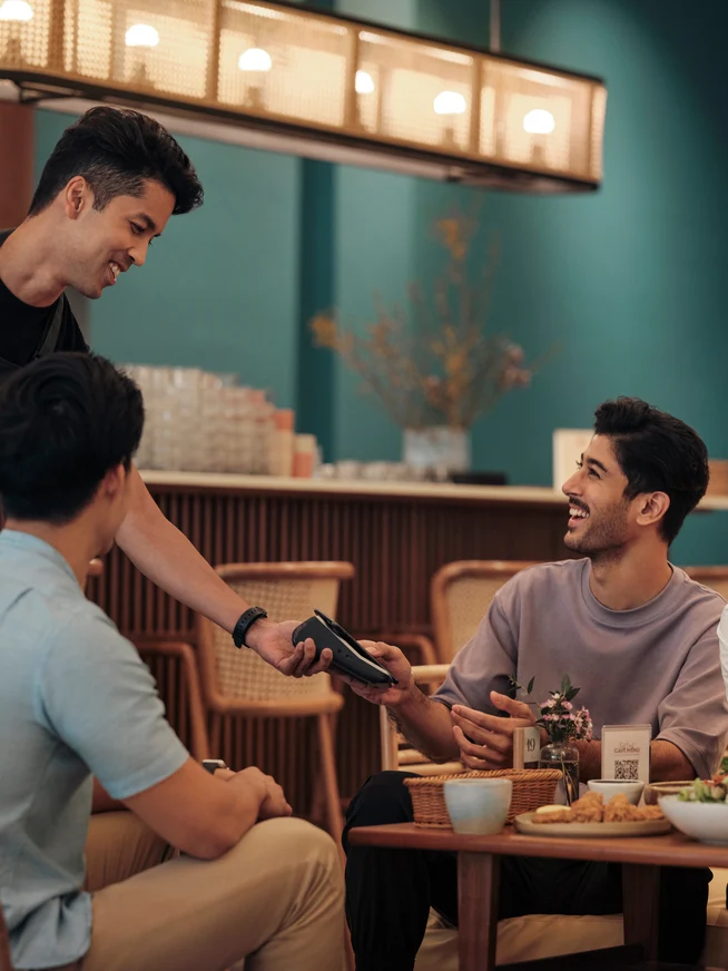 A man at a restaurant counter, paying for his order by tapping his phone on Adyen’s V400m terminal.