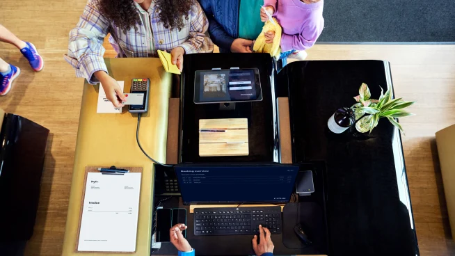 Una familia en el mostrador de recepción de un hotel realizando un pago tocando una tarjeta en el terminal P400 Plus de Adyen.