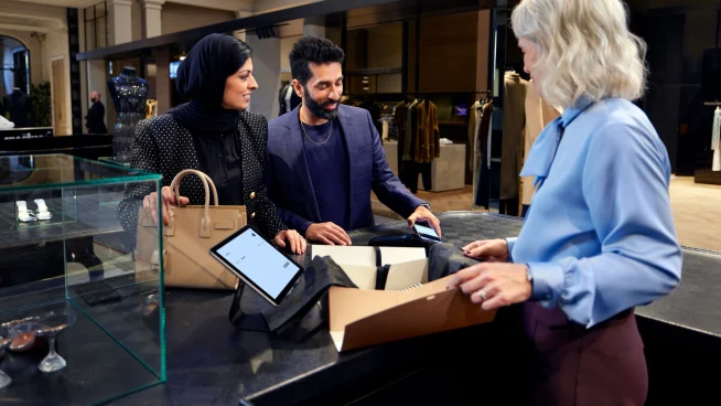 A couple in a luxury fashion store paying for their purchase by tapping their iPhone at Adyen's S1F2 terminal.