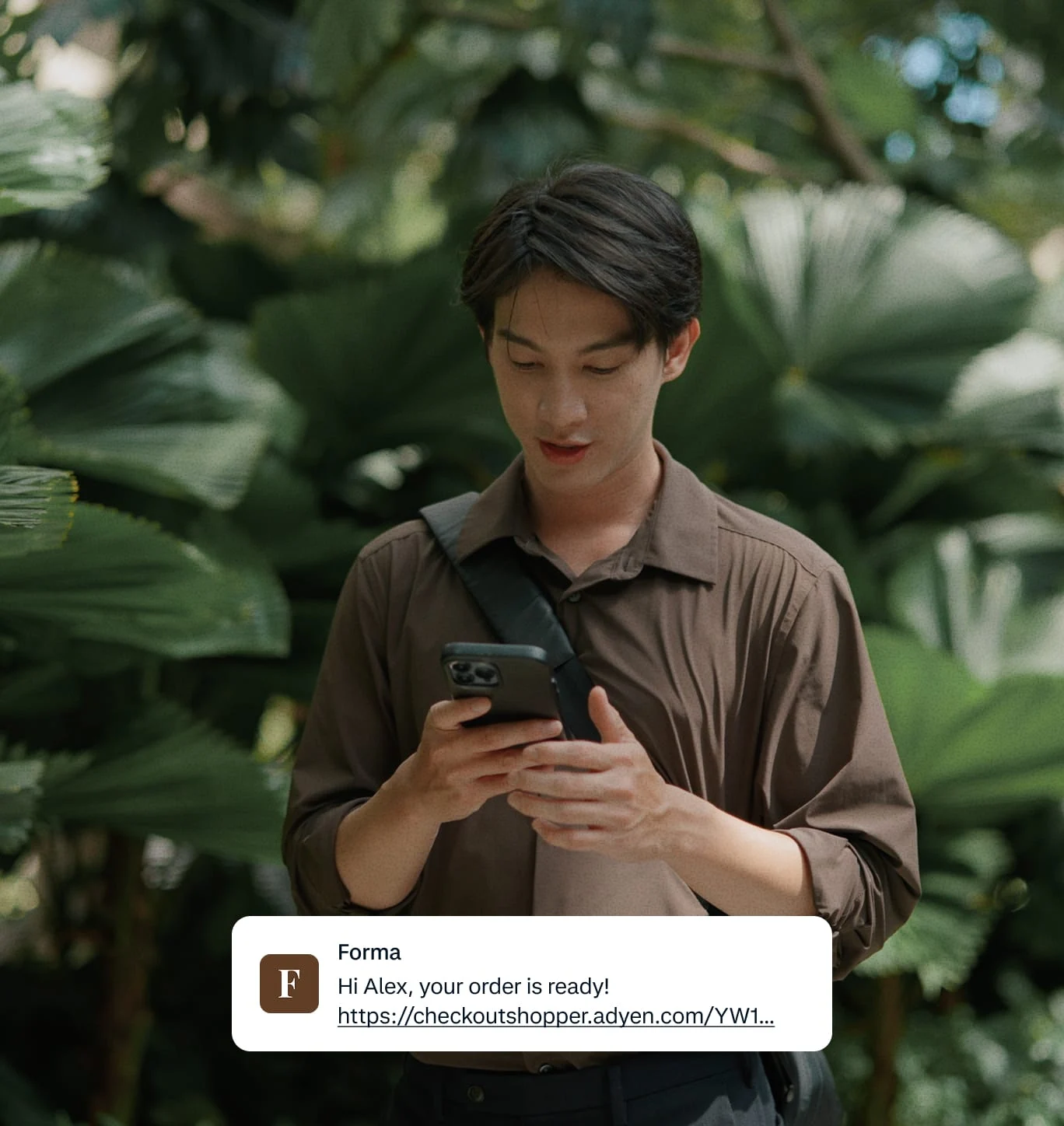 A person using a smartphone outdoors, with a notification about order confirmation from Adyen.