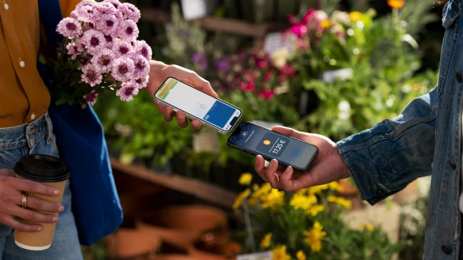 A customer in an Italian flower shop tapping their iPhone at the seller's iPhone to pay for the purchase.