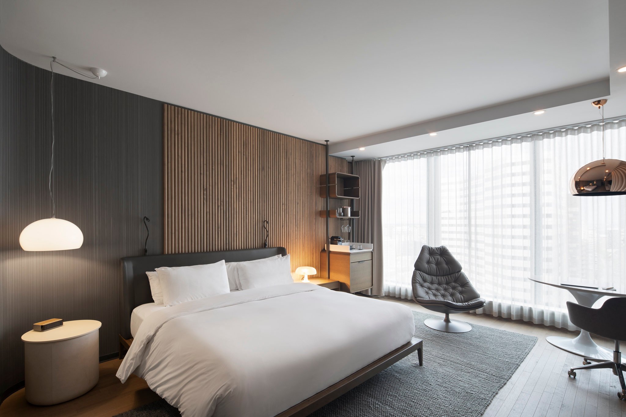 A modern hotel room with a bed, seating area, and large window with sheer curtains