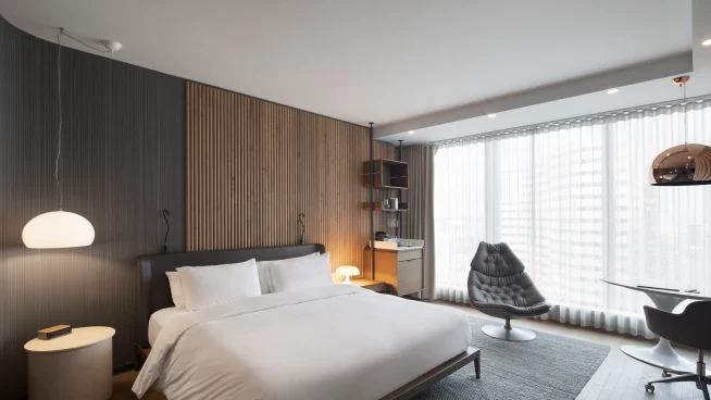 A modern hotel room with a bed, seating area, and large window with sheer curtains