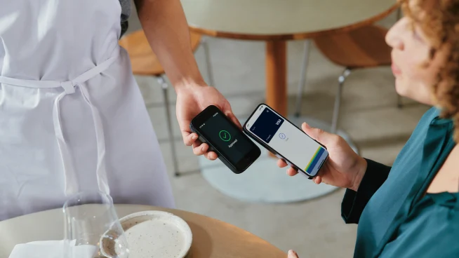 A woman in restaurant paying for food by tapping a smartphone on Adyen's AMS1 terminal.