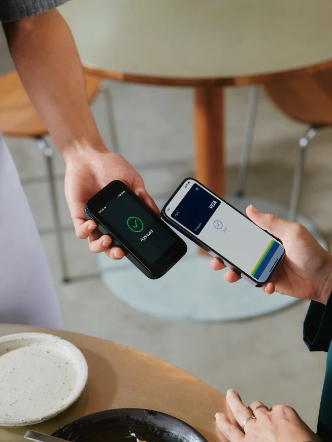 A woman in restaurant paying for food by tapping a smartphone on Adyen's AMS1 terminal.