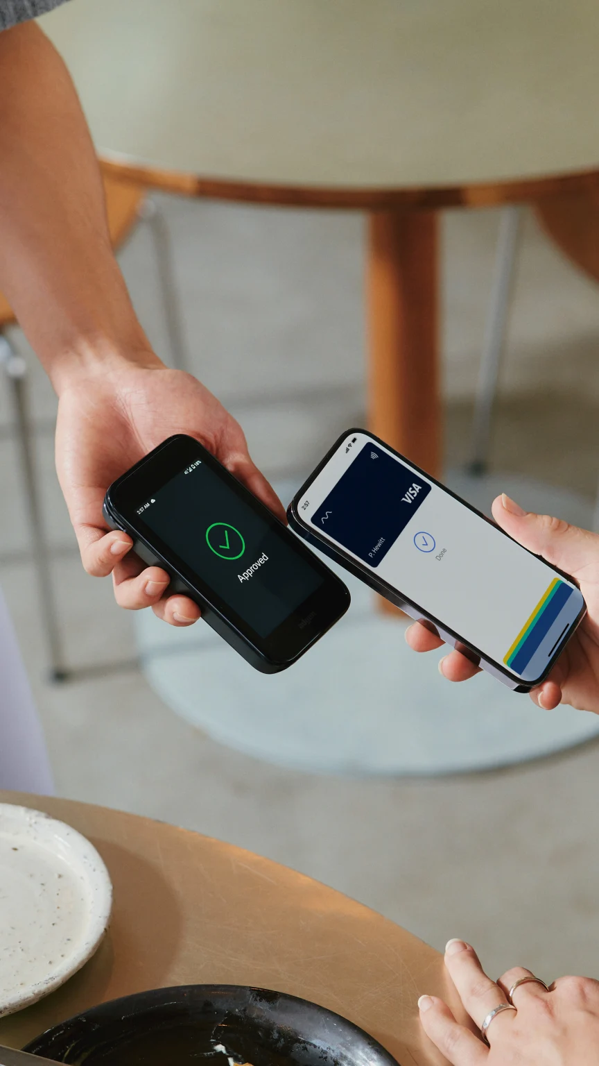 A woman in restaurant paying for food by tapping a smartphone on Adyen's AMS1 terminal.