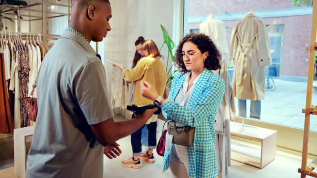 Uma mulher em uma loja de roupas pagando ao tocar seu Apple Watch no terminal S1F2 da Adyen.