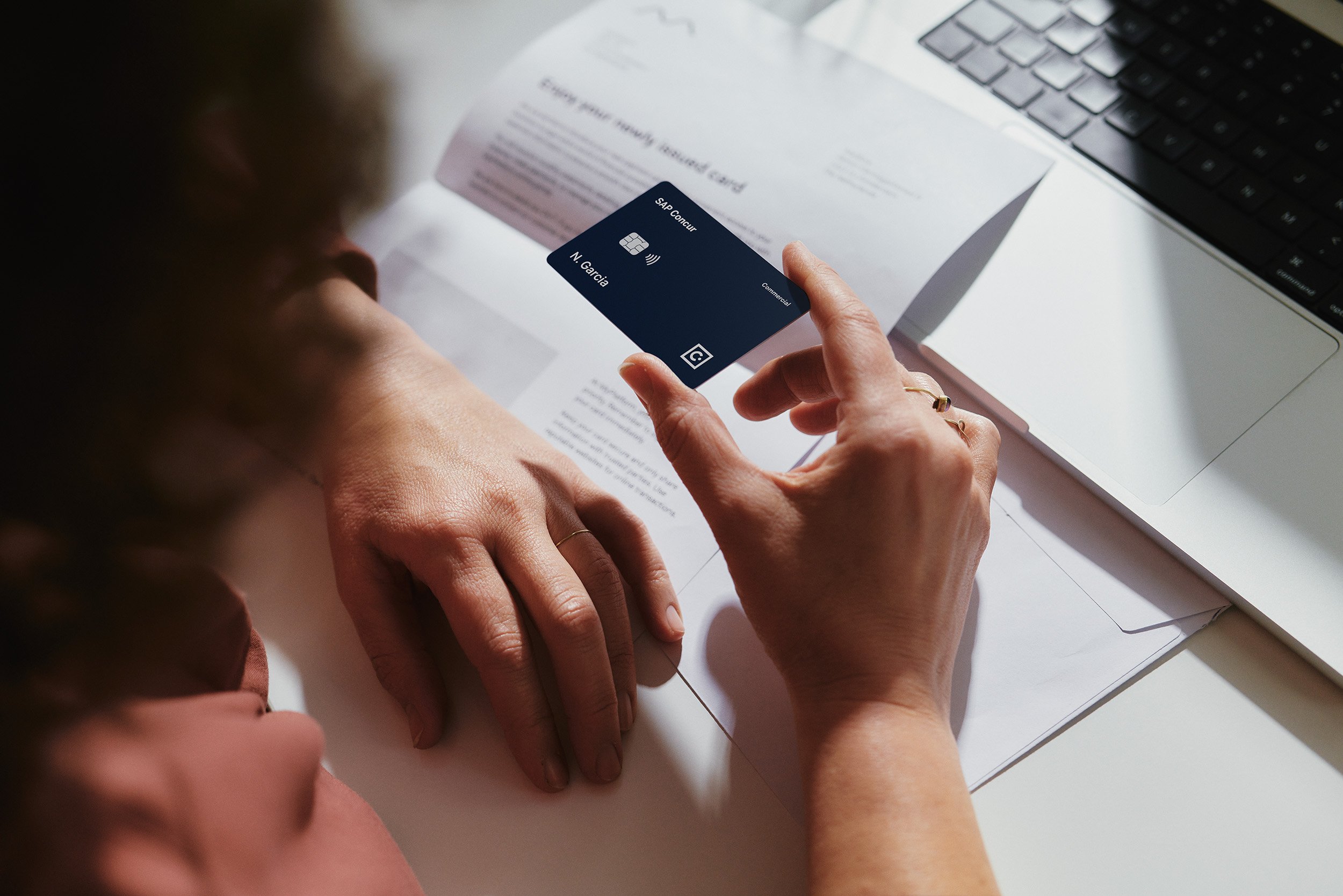 Person using a mobile payment terminal with a laptop and documents on the desk