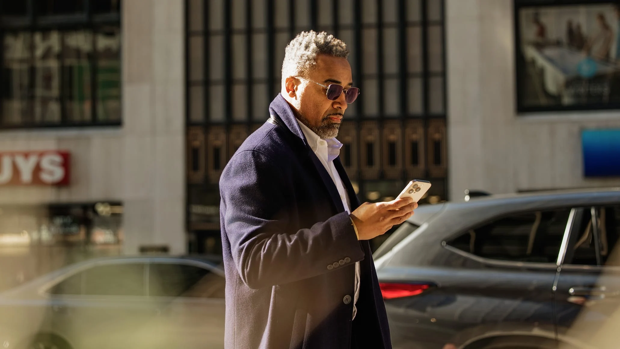 A man using a smartphone outdoors, with a car and a building in the background, payment provided by an Adyen terminal.