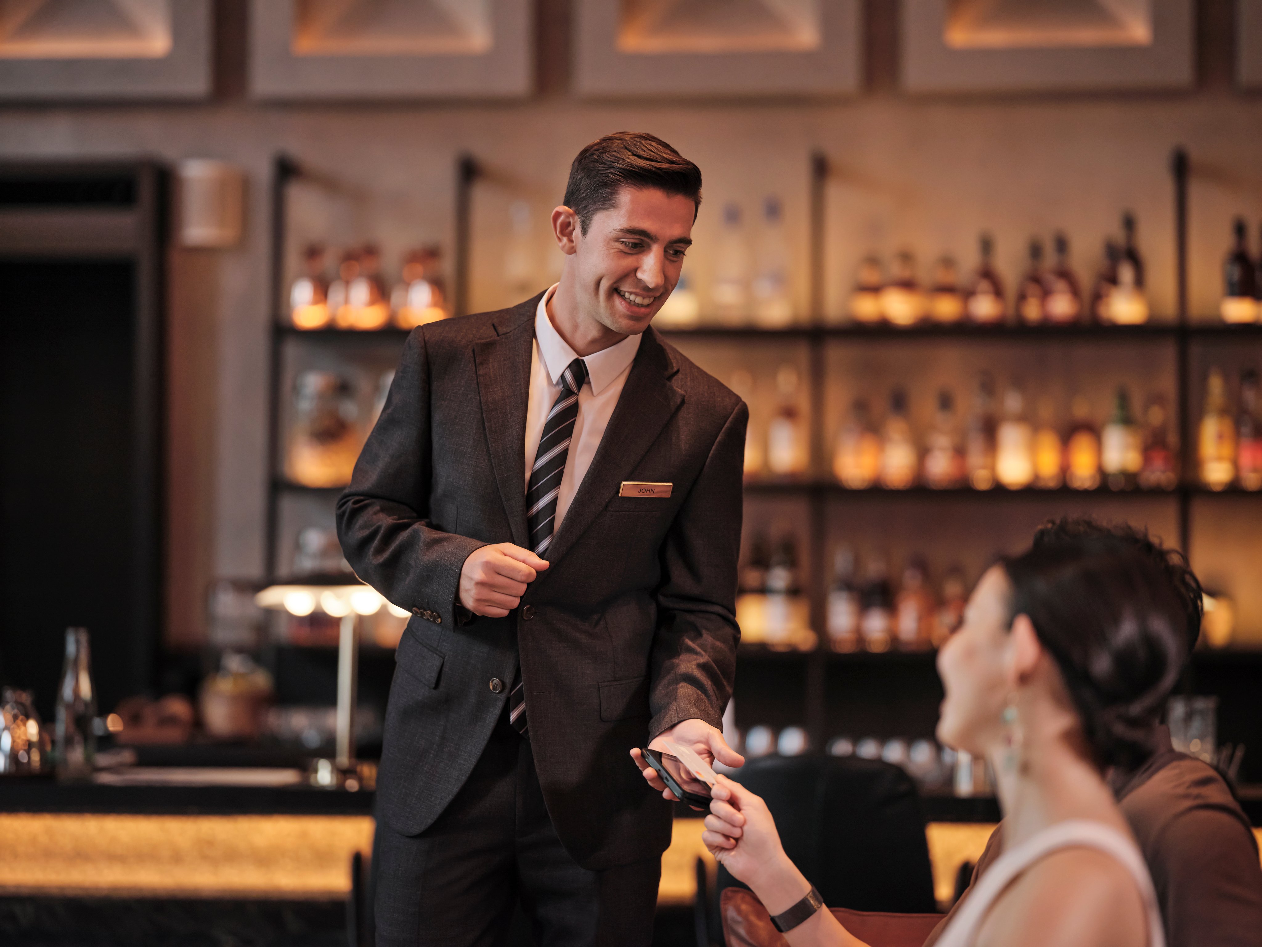 A woman in a hotel bar paying for their drinks by tapping a card on Adyen's terminal.