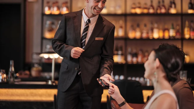 Uma mulher em um bar de hotel pagando suas bebidas tocando um cartão no terminal da Adyen.