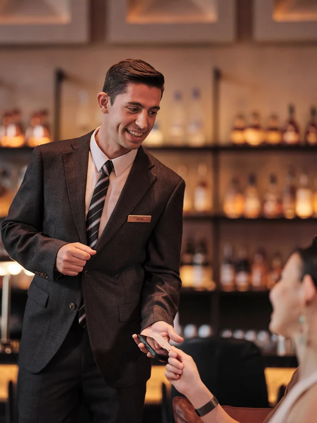 A woman in a hotel bar paying for their drinks by tapping a card on Adyen's terminal.