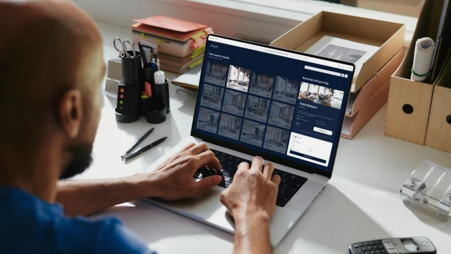 Un hombre frente a una laptop, realizando una reserva de hotel mediante un sistema de reserva de agencia de viajes en línea (OTA).