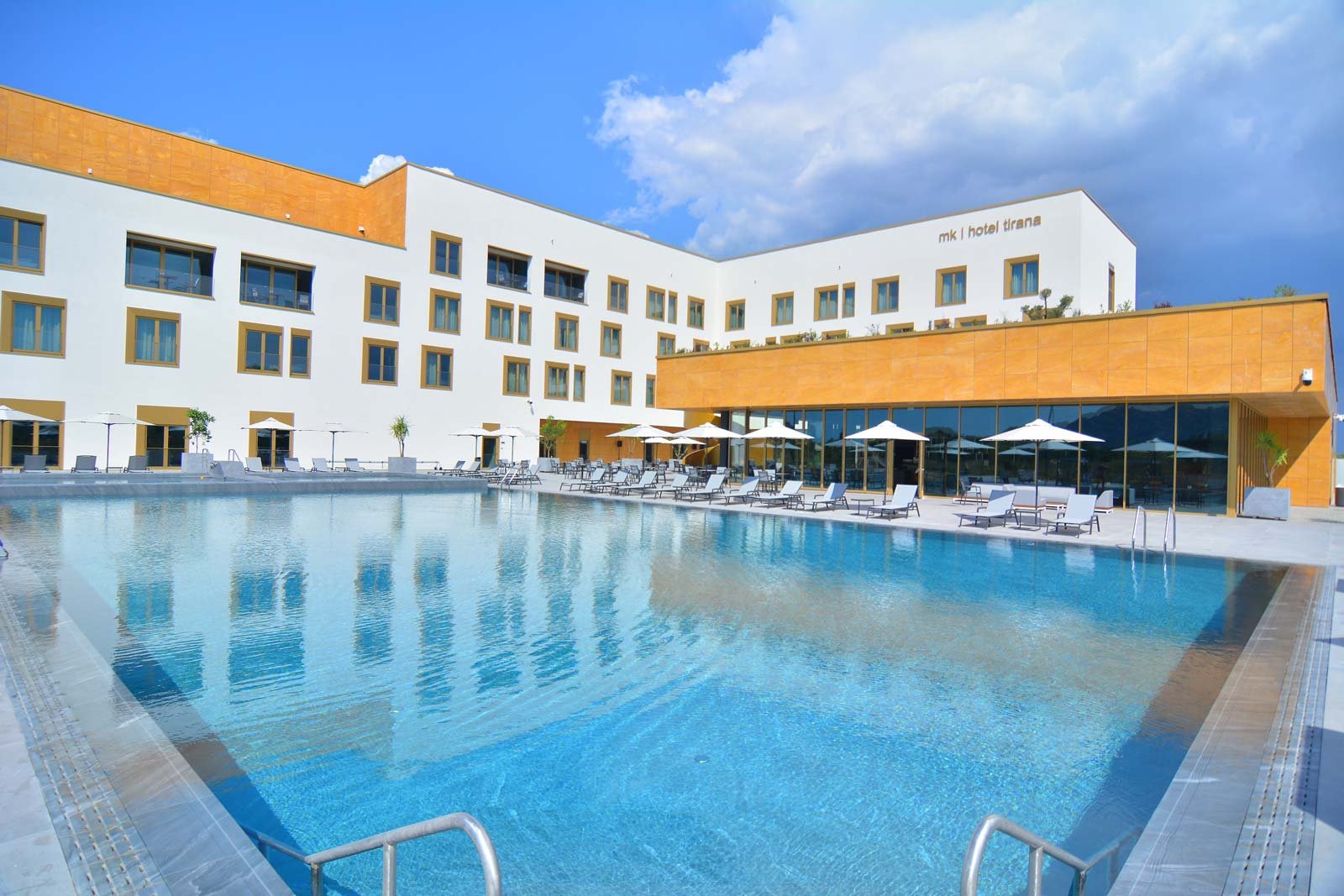 MK Hotel Gebäude mit großem Swimmingpool und Liegestühlen unter blauem Himmel