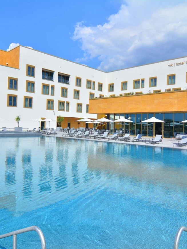 MK Hotel Gebäude mit großem Swimmingpool und Liegestühlen unter blauem Himmel