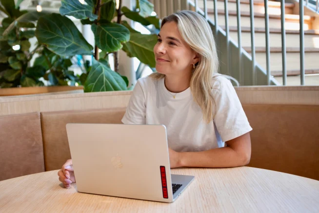 A woman working on a laptop at a table in a modern office space.