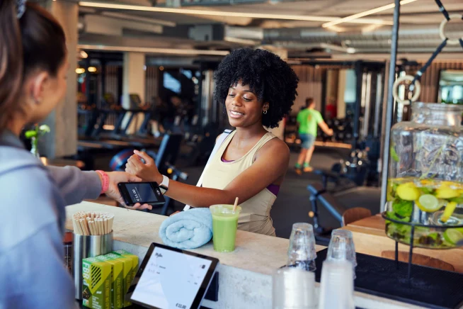Une femme à la salle de sport payant en tapant sa montre Apple sur le terminal S1E d'Adyen.