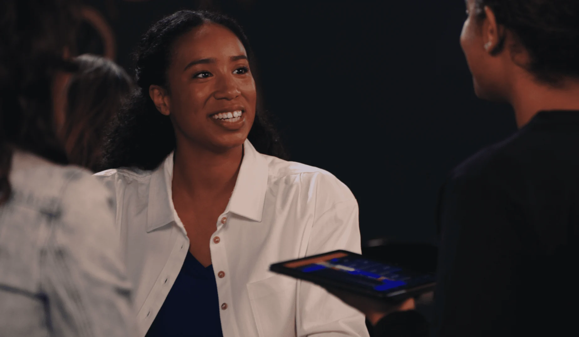 Mulher sorridente engajada em conversa com colegas usando um tablet com aplicação de pagamento.