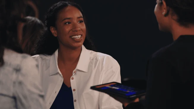 Mulher sorridente engajada em conversa com colegas usando um tablet com aplicação de pagamento.