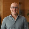 Dipendente Adyen sorridente in ufficio, con parete in legno e piante sullo sfondo.