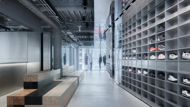 Modern shoe store interior with sneakers displayed on shelves and customers walking.