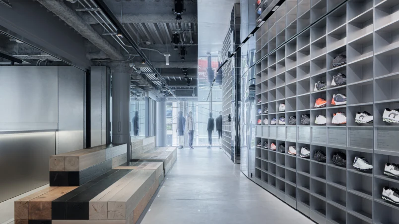Modern shoe store interior with sneakers displayed on shelves and customers walking.