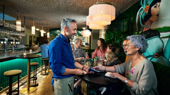 En kvinde i en restaurant betaler ved at tappe sin kort på Adyens V400m-terminal.