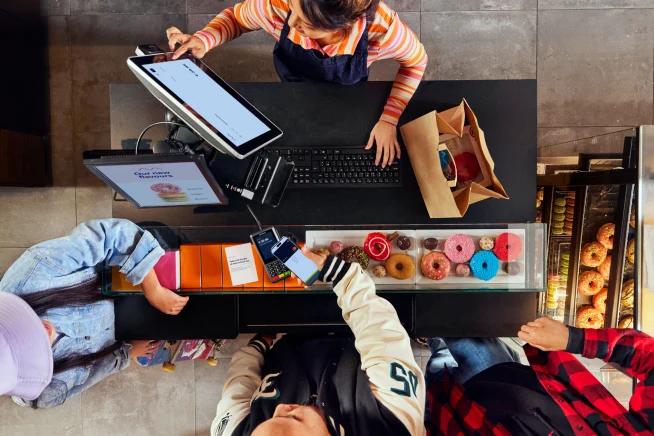 A young man paying at a donut shop by tapping his smartphone on Adyen's P400 terminal.