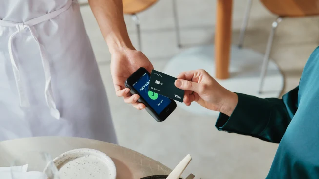 A woman in restaurant paying for food by tapping a VISA card on Adyen's AMS1 terminal.