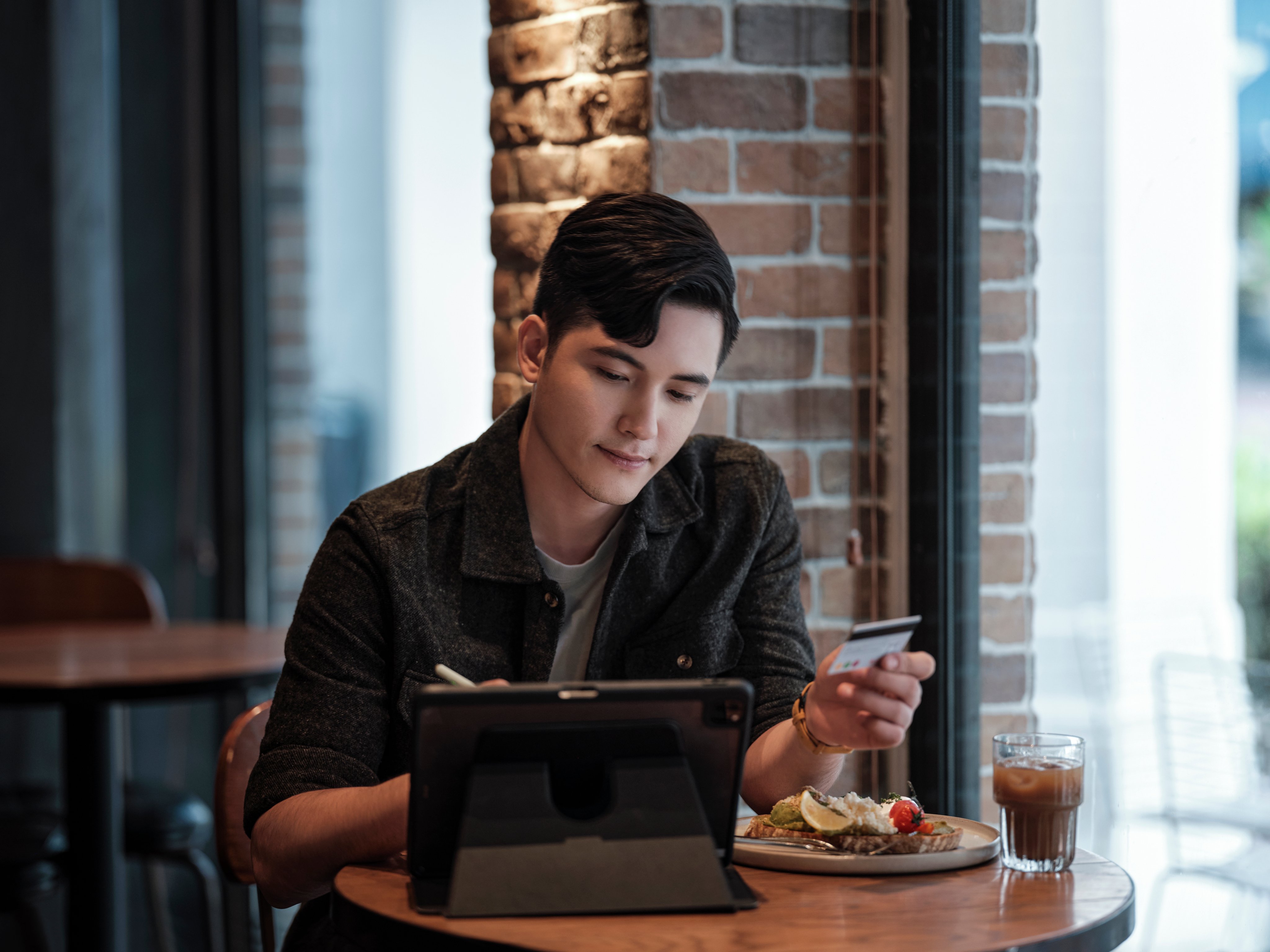 A man in a restaurant behind his iPad holding a payment card