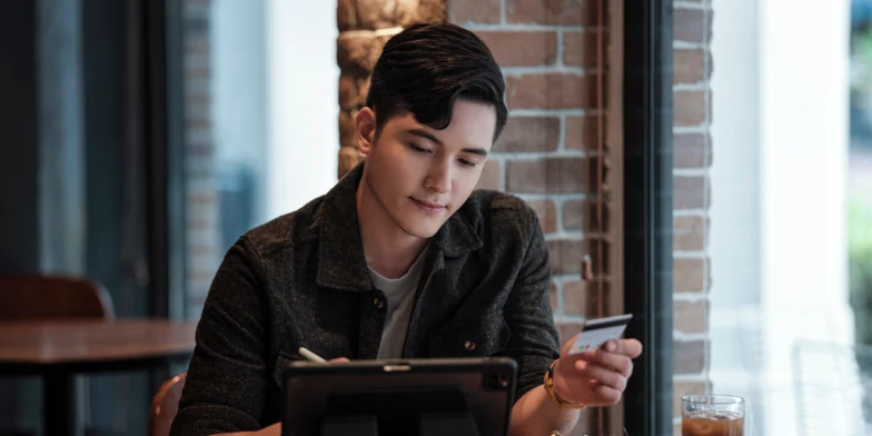 A man in a restaurant behind his iPad holding a payment card
