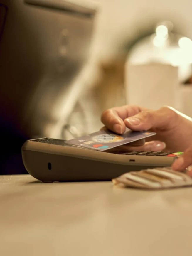 Primer plano de un pago sin contacto en proceso con una tarjeta y un terminal POS.