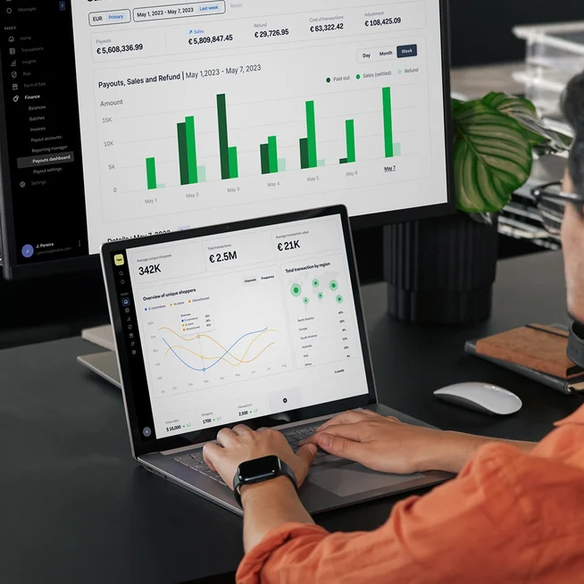 Personne analysant des données financières sur les écrans Adyen UI affichés sur les moniteurs d'ordinateur et de tablette.