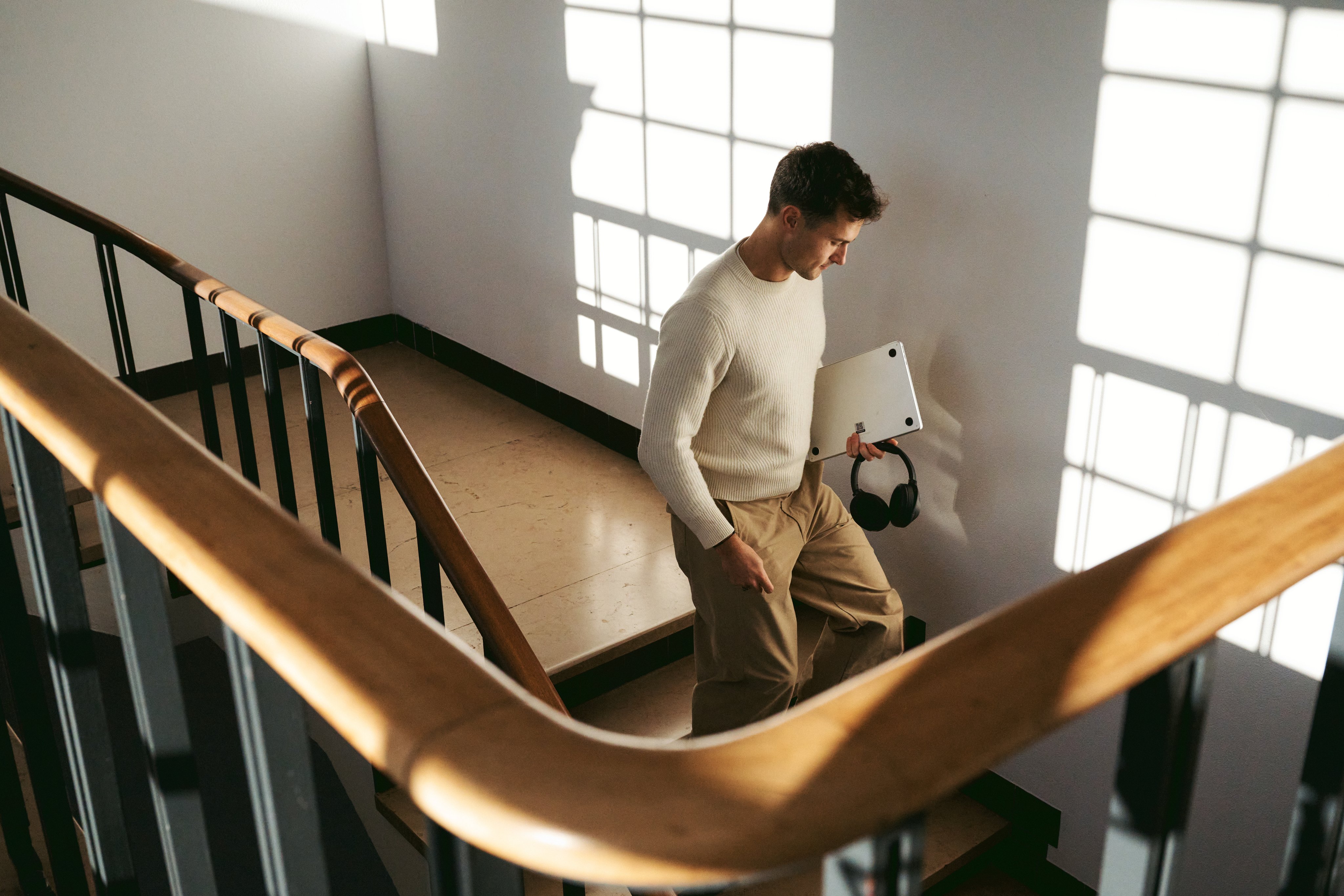 man walking down the stairs with a laptop and headphones in his hand
